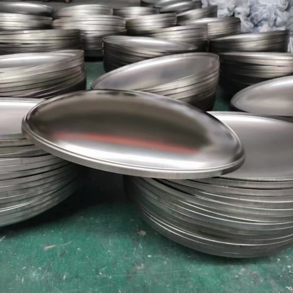 Stainless steel pressure vessel heads in a workshop, showing formed dished heads manufactured for tanks and industrial equipment.