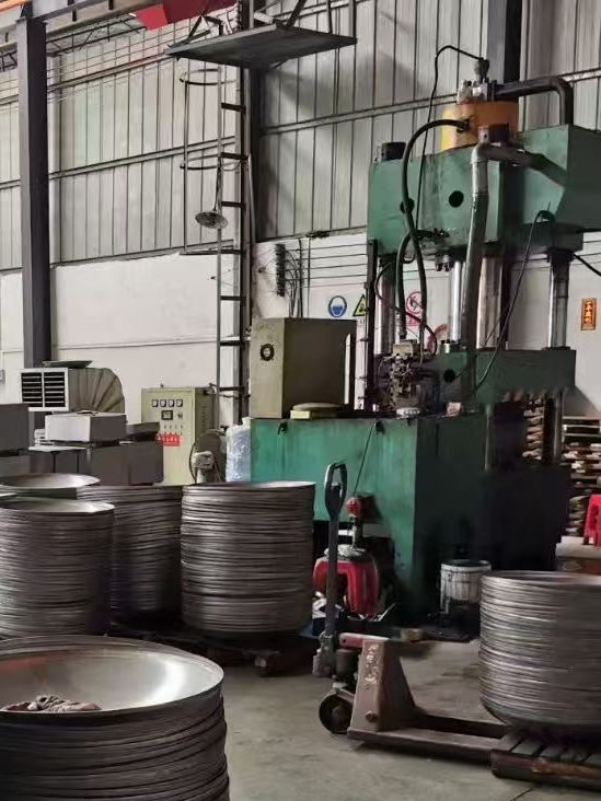 Hydraulic press forming stainless steel components and pressure vessel heads for custom industrial fabrication.