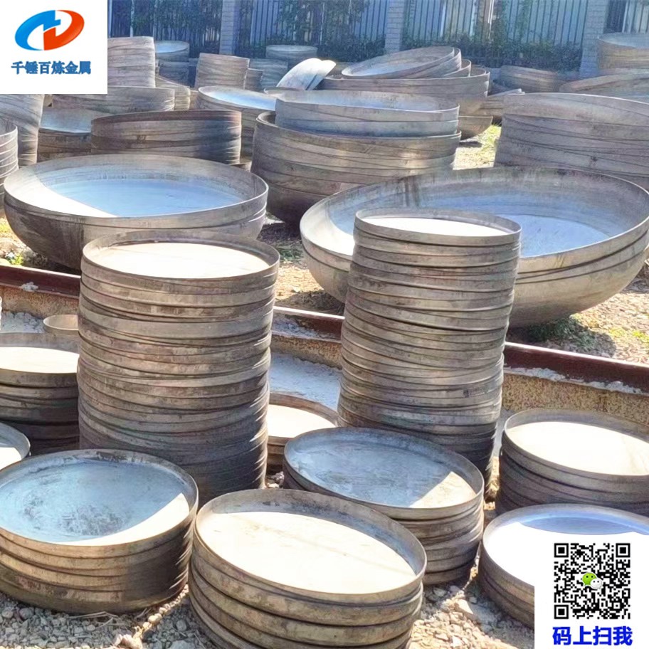 Stainless steel flat heads in multiple diameters stacked in a fabrication workshop for tank and vessel manufacturing.