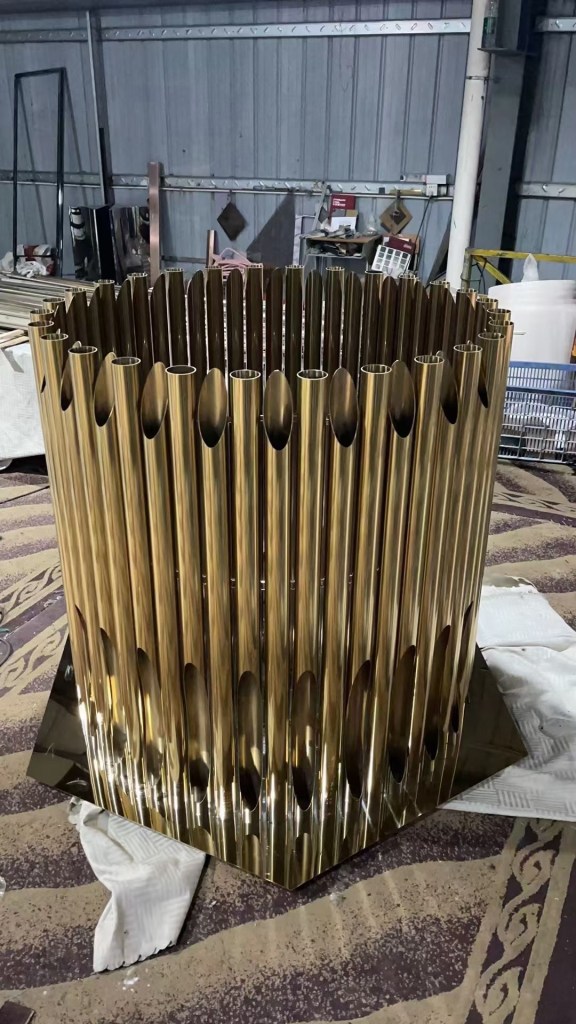 Custom gold-colored stainless steel components formed from repeated curved metal profiles, fabricated and assembled for architectural features and decorative metal installations.