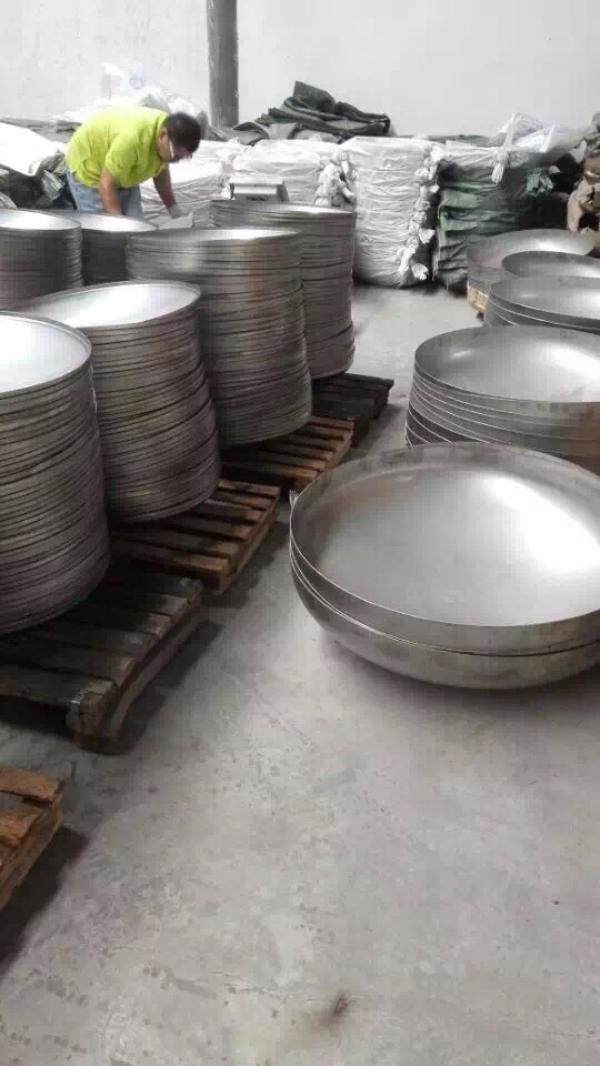 Multiple stainless steel hemispherical heads stacked in a fabrication workshop, showing different sizes of formed heads for pressure vessels and tanks.