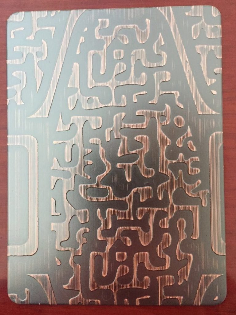 Copper-toned stainless steel sheet with large abstract geometric etched patterns in contrasting silver and rose copper tones for decorative metal panels and custom surface finishing.