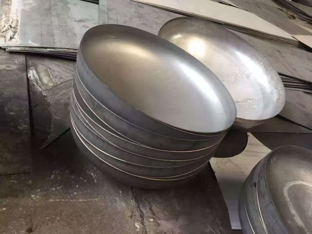 Stacked stainless steel elliptical heads with smooth formed surfaces and rounded profiles for tanks and industrial pressure vessels.