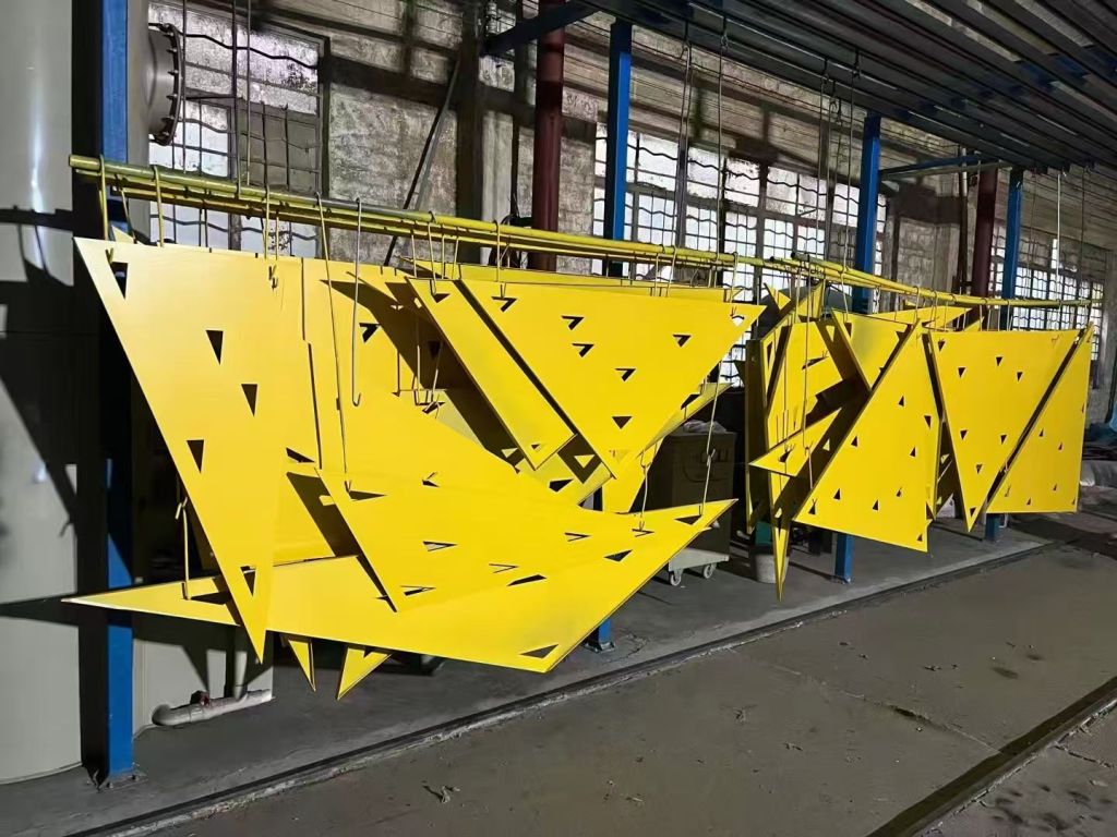 Yellow powder-coated metal components hanging on a coating line, showing custom color and surface appearance options for fabricated metal products.