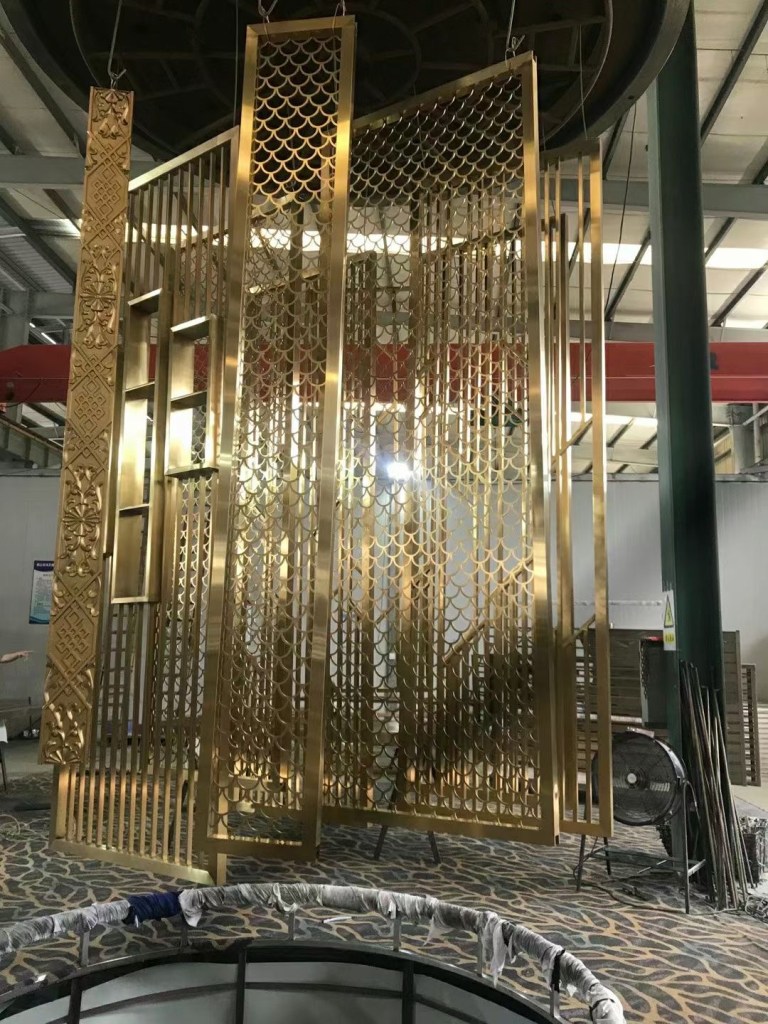 Custom gold-colored stainless steel screen with geometric lattice patterns and decorative metal frames, fabricated for interior partitions and architectural space dividers.