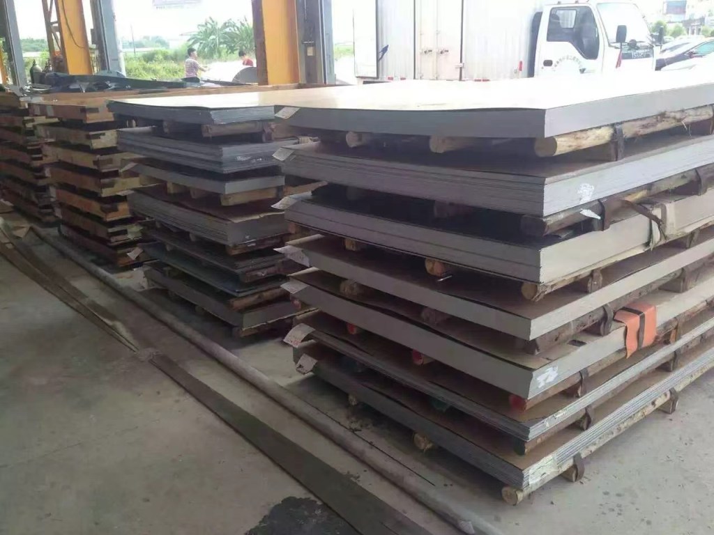Stacks of rectangular stainless steel sheets in different sizes and thicknesses stored horizontally in a workshop, representing material grade, sheet dimensions, thickness and quantity for surface finishing projects.