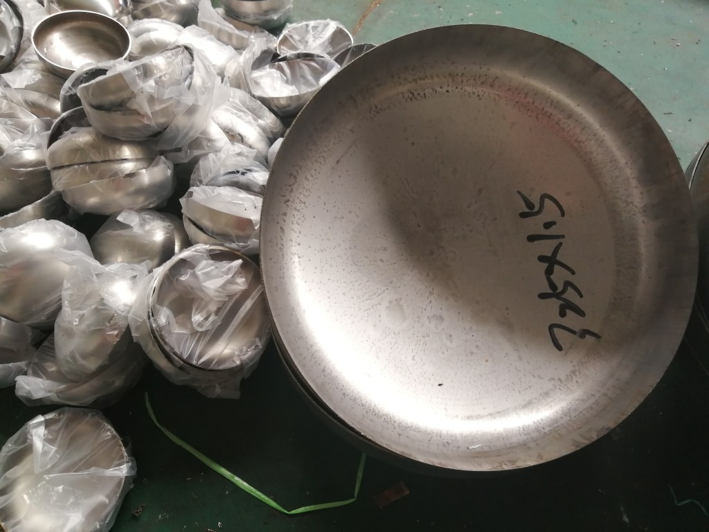 Single stainless steel elliptical head showing a circular edge and shallow ellipsoidal curved profile for pressure vessel fabrication.