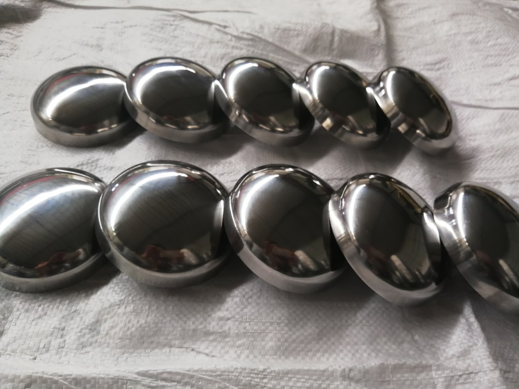 Multiple stainless steel elliptical heads with smooth curved profiles arranged in rows for pressure vessel and tank fabrication.