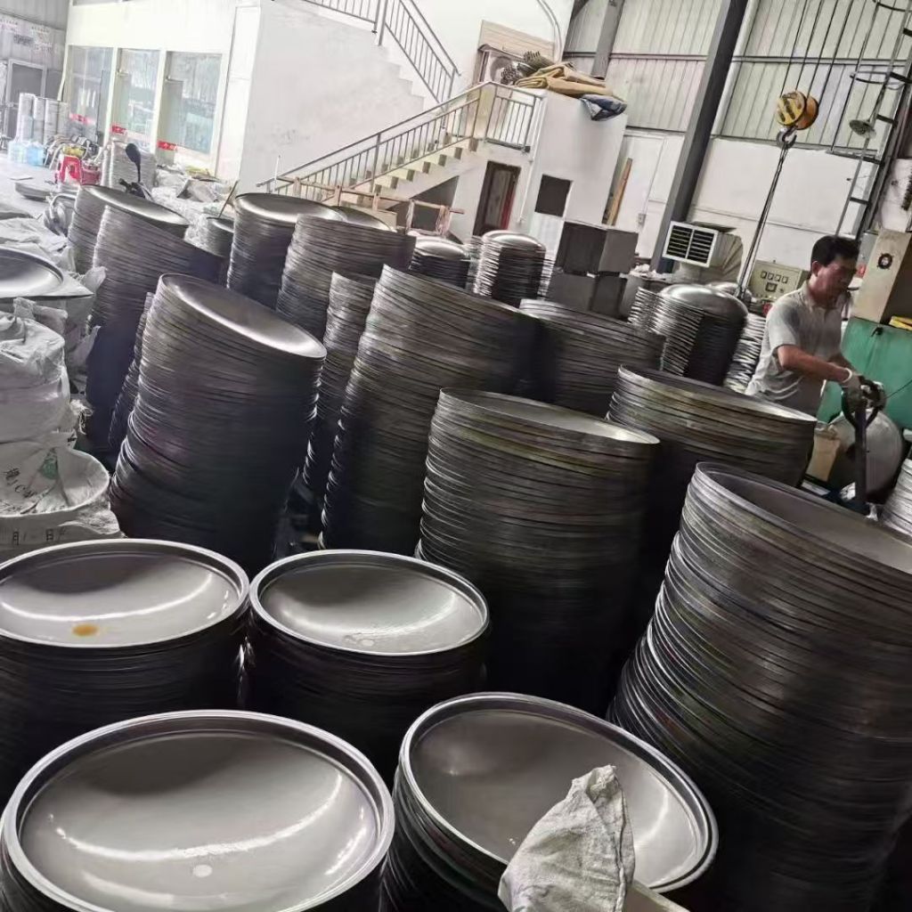 Large quantities of stainless steel dished heads in different diameters stacked in a fabrication workshop for tanks and industrial vessels.