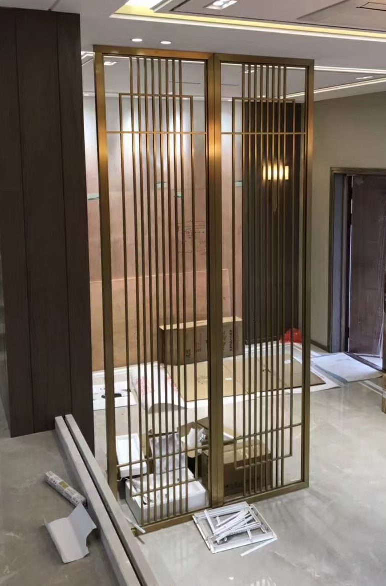 Custom gold-colored stainless steel partition with vertical metal profiles installed in a modern interior, designed as an architectural screen and decorative space divider.