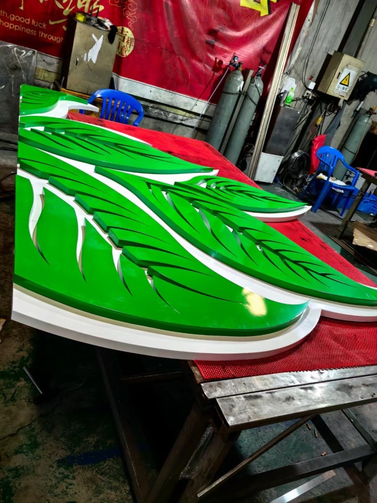 Custom green and white decorative metal components with curved leaf-shaped forms, fabricated and finished for colorful architectural and decorative metalwork applications.